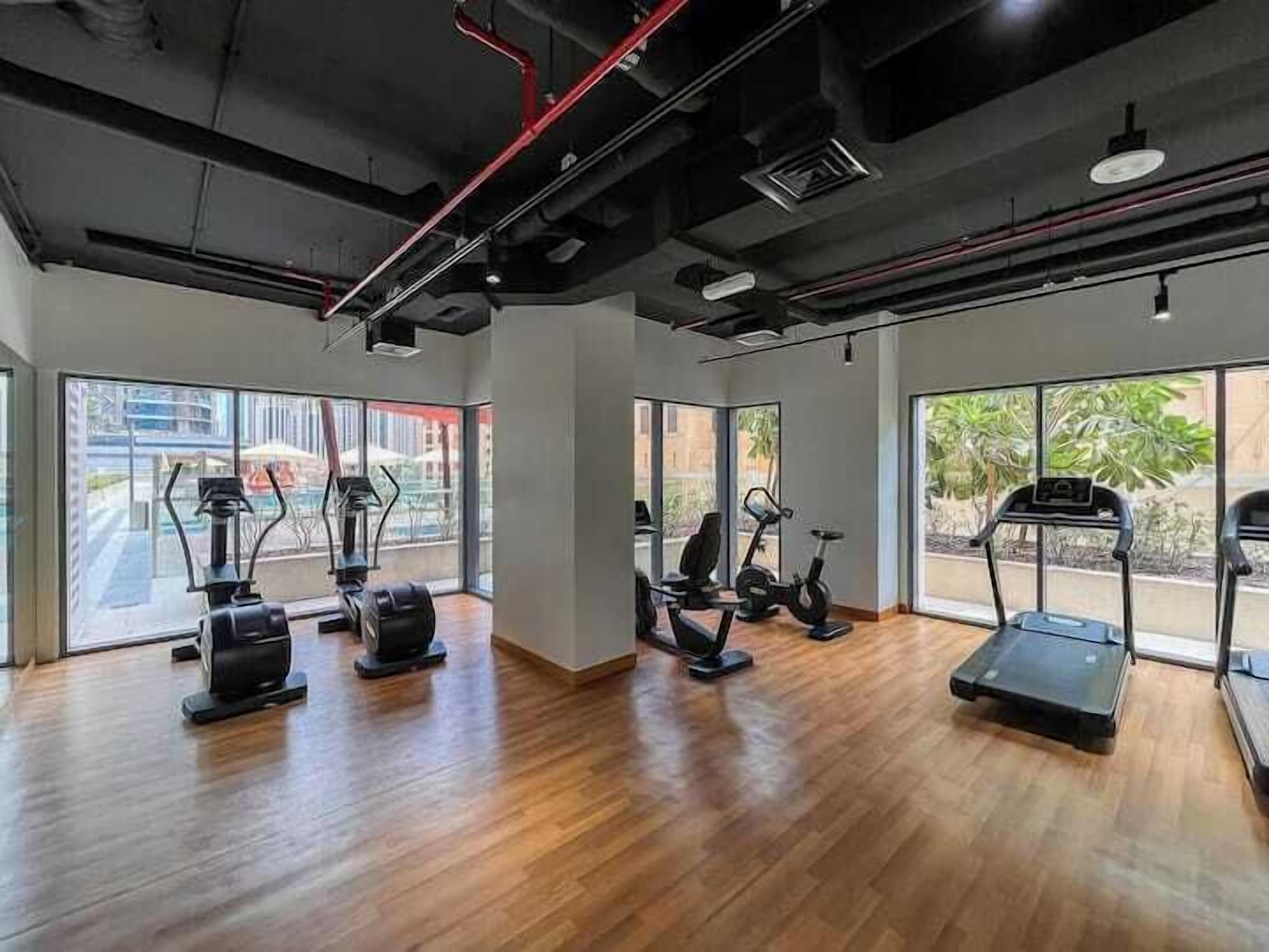 Uma academia com equipamentos de ginástica, grandes janelas e piso de madeira.