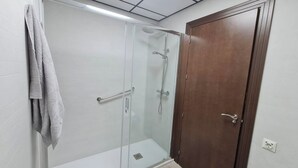 A glass-enclosed shower with a handheld showerhead and a handheld faucet.