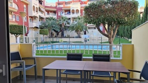A balcony with a table and chairs, overlooking a swimming pool and a residential area with multi-story buildings.