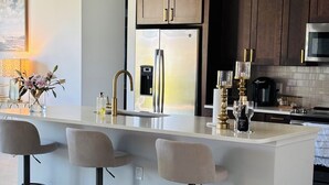 A modern kitchen with a central island, bar stools, a stainless steel refrigerator, and dark wooden cabinets. - New- Villa white Peacock Exclusive Villa with all amenities, top location (Cape Coral)