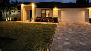 A residential house with a paved driveway, a well-maintained lawn, and a garage. - New- Villa white Peacock Exclusive Villa with all amenities, top location (Cape Coral)