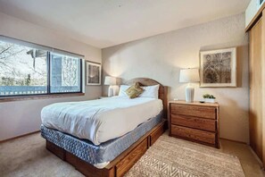 A bedroom with a large bed, a nightstand, a dresser, and a window with a view.