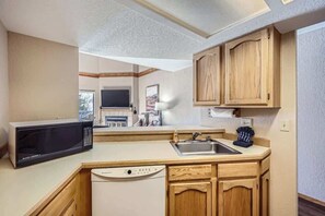 Una cocina compacta con armarios de madera, microondas, lavavajillas y un lavabo.