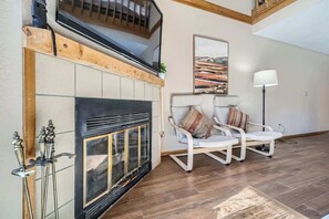 A living room with a fireplace, a television mounted above it, and a modern chair with cushions.