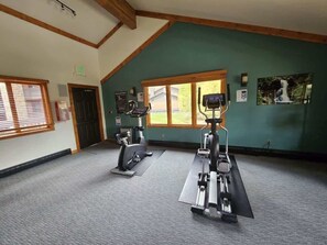 Un gimnasio con dos cintas de correr, un ventanal grande y una pared verde.