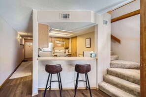 A compact kitchen with a central island, two bar stools, and a staircase to the right.