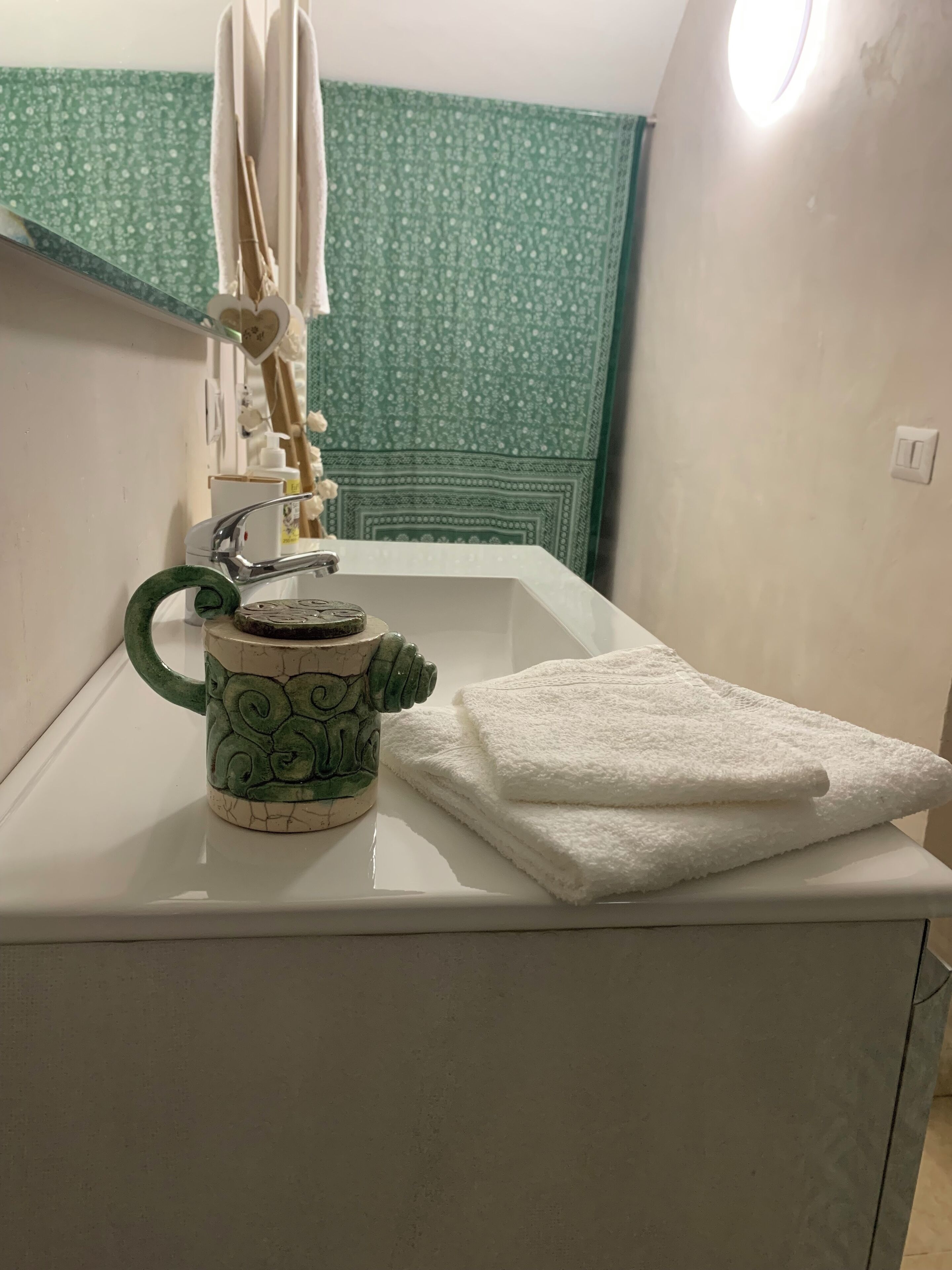 A bathroom with a white sink, a green decorative mug, and a white towel on the counter.