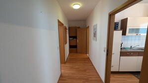 A narrow hallway with wooden flooring leading to a kitchen area with white cabinets and a stainless steel sink. - Comfort apartment for 4 guests in Chemnitz K1R (Chemnitz)