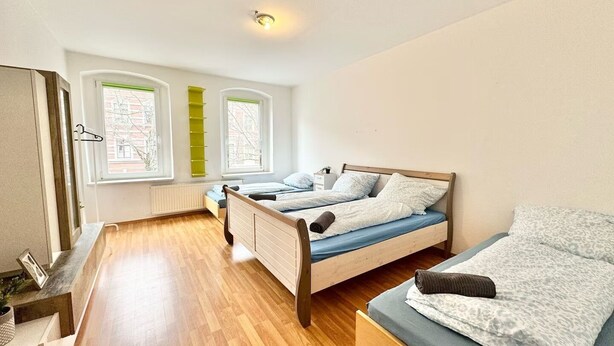 A bedroom with a wooden bed, a sofa, and a window with a view of buildings. - Comfort apartment for 4 guests in Chemnitz K1R (Chemnitz)