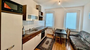 A compact kitchen with a microwave, sink, and cabinets. There is a dining table with chairs and a sofa in the adjacent living area. - Comfort apartment for 4 guests in Chemnitz K1R (Chemnitz)