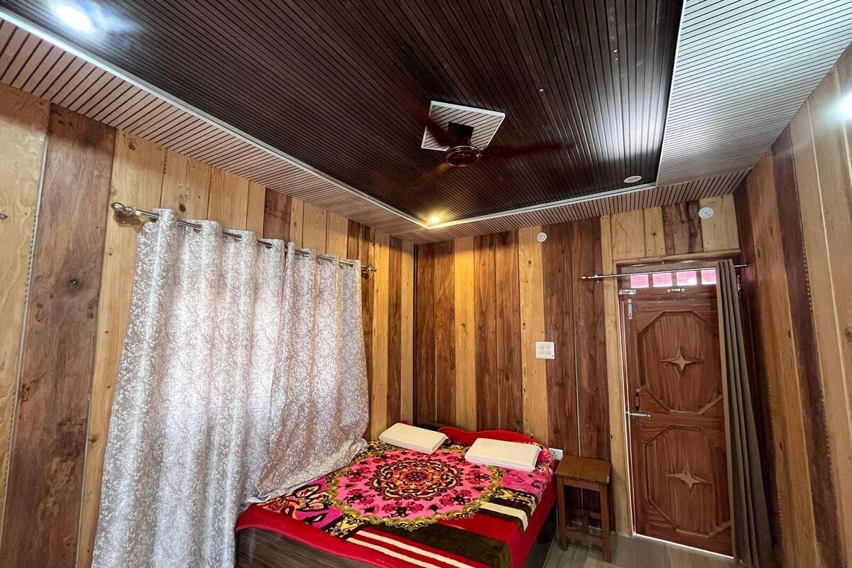 Ein Schlafzimmer mit Holzwänden, einem Deckenventilator, einem Bett mit gemustertem Überwurf und einer Holztür.
