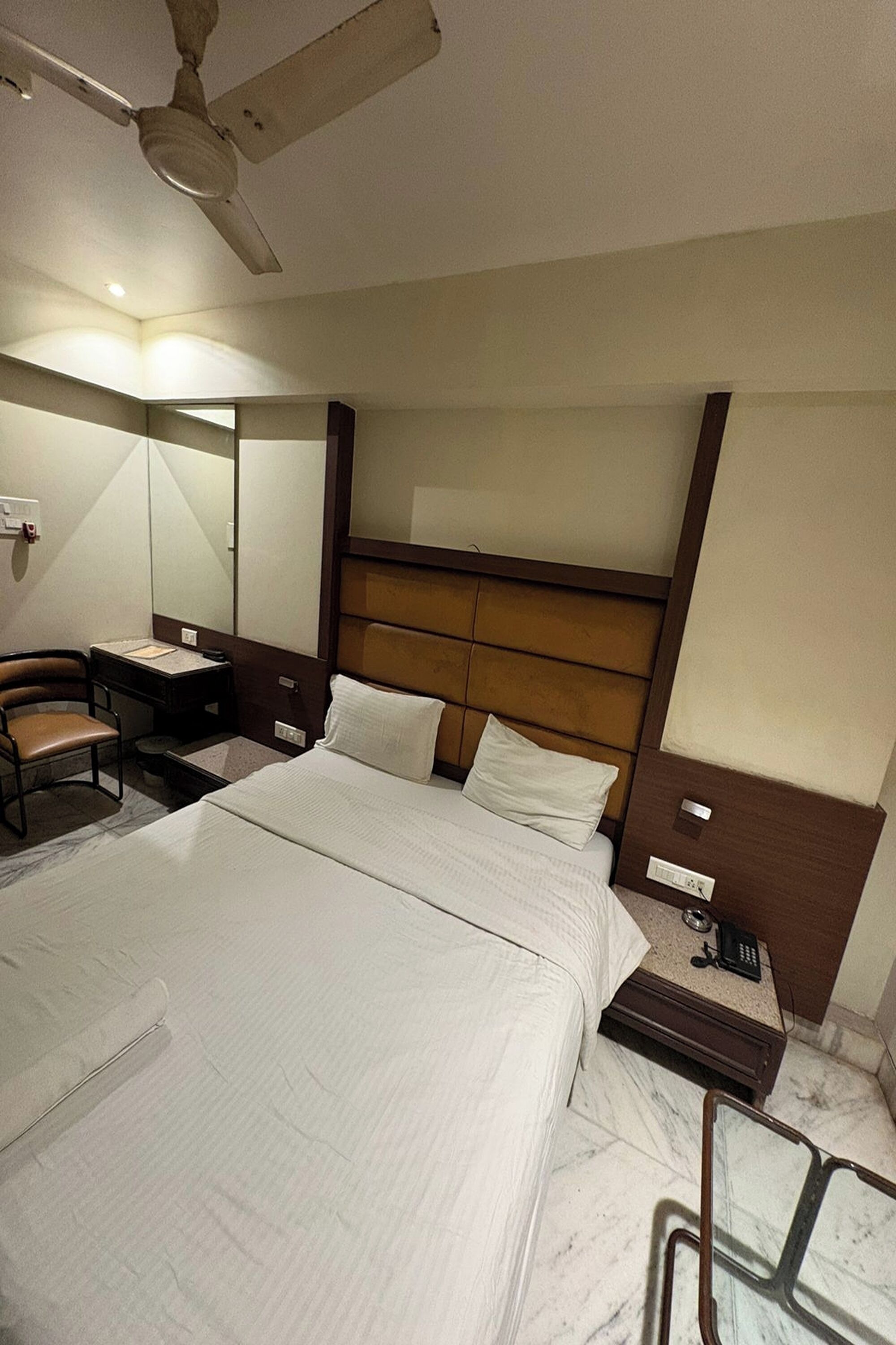 Camera d'albergo con un letto grande, una scrivania con sedia, un comodino con telefono e una ventola a soffitto.
