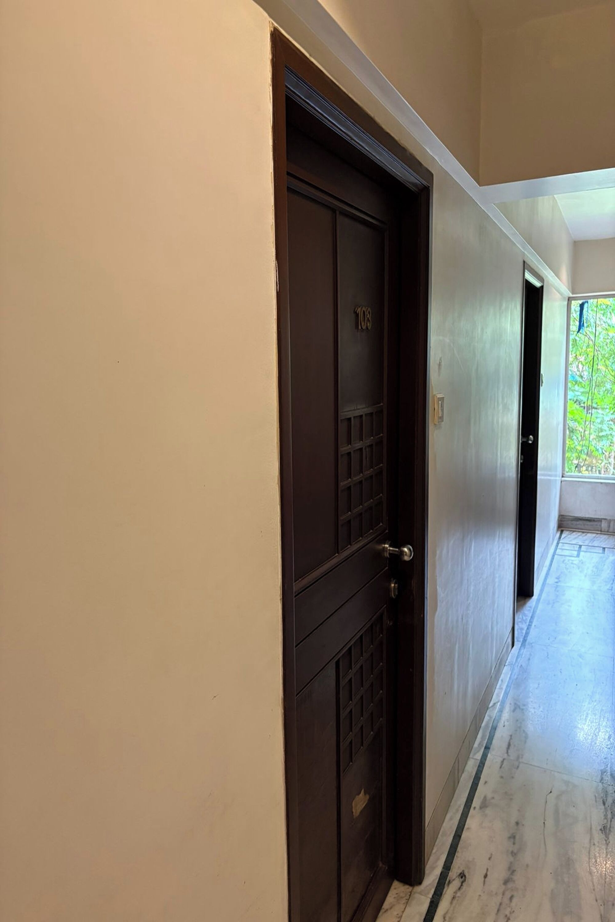 A hallway with a dark wooden door, beige walls, and a marble floor.