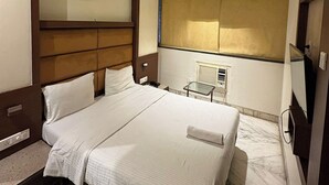 A hotel room with a large bed, a ceiling fan, a small table, and a large mirror. - Pravasi Residency (Mumbai)