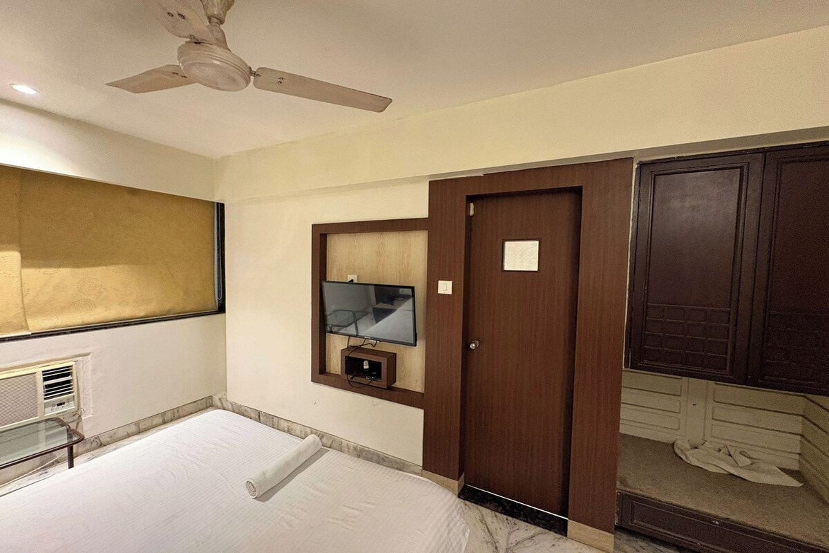A hotel room with a bed, a ceiling fan, a television mounted on the wall, and a wardrobe.