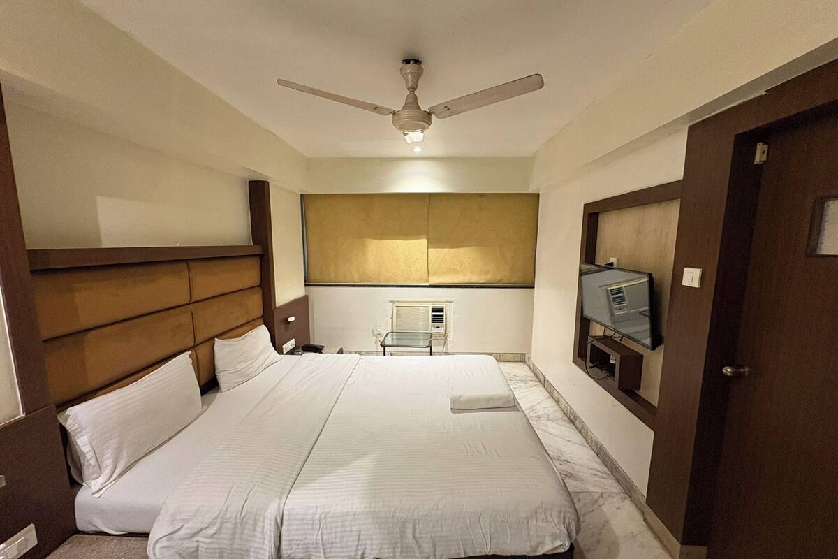 A hotel room with a large bed, a ceiling fan, a television, and a minibar.