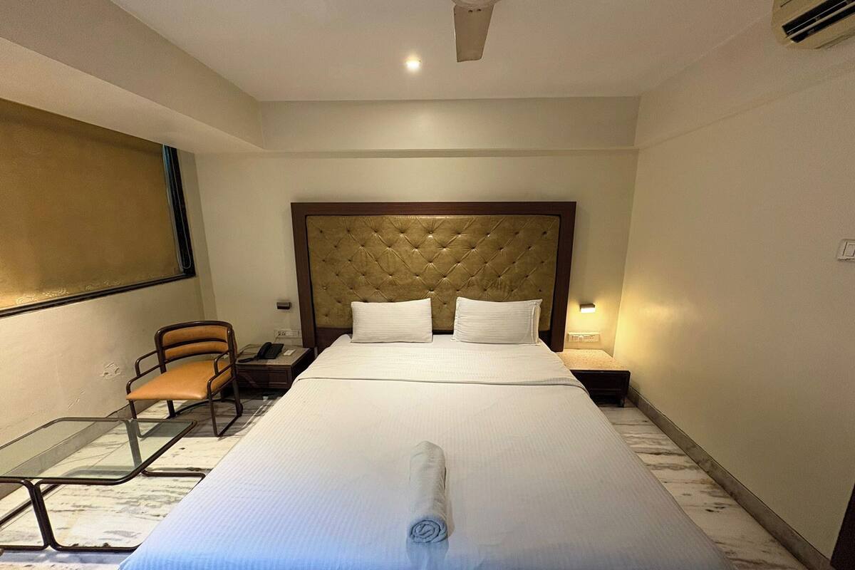 A hotel room with a large bed, a headboard, a bedside table, a chair, and a glass table.