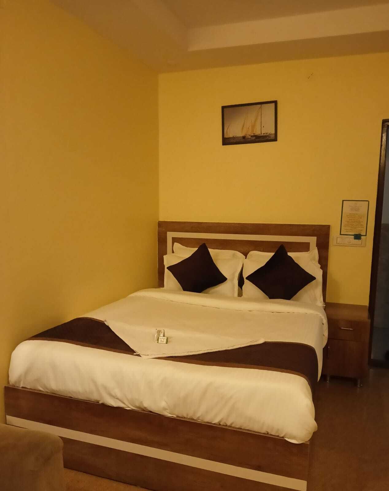 A bed with white and brown bedding, two dark pillows, and a small bedside table with a lamp.
