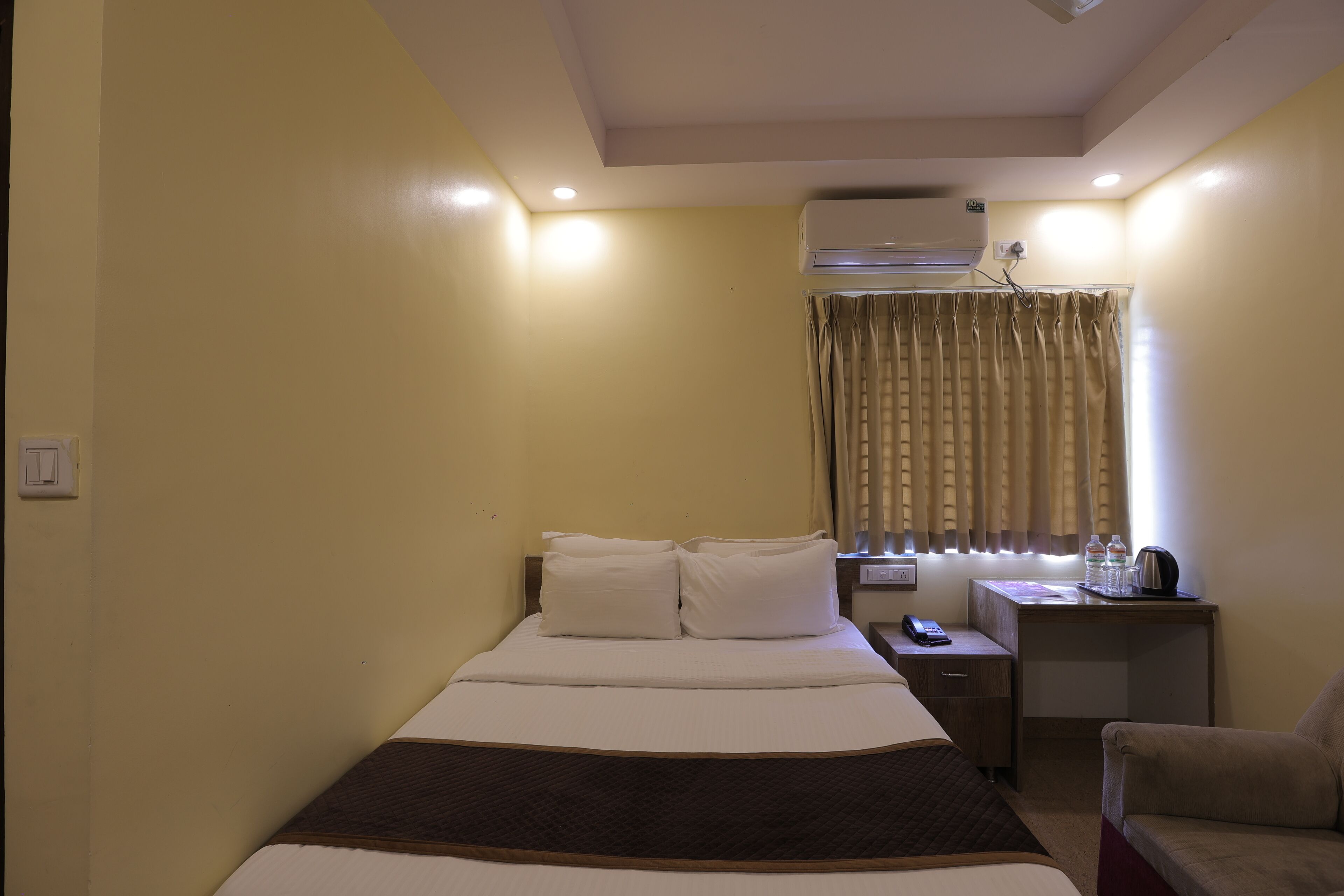Una habitación de hotel con cama, mesita de noche, silla y aire acondicionado.