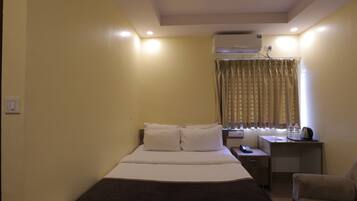 Una habitación de hotel con cama, mesita de noche, silla y aire acondicionado.