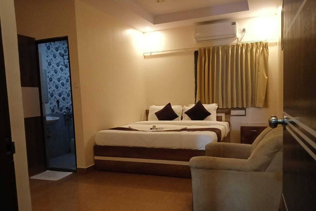 Une chambre d’hôtel équipée d’un lit, d’une chaise, d’un bureau, d’un climatiseur et d’une salle de bain visible à travers une porte vitrée.