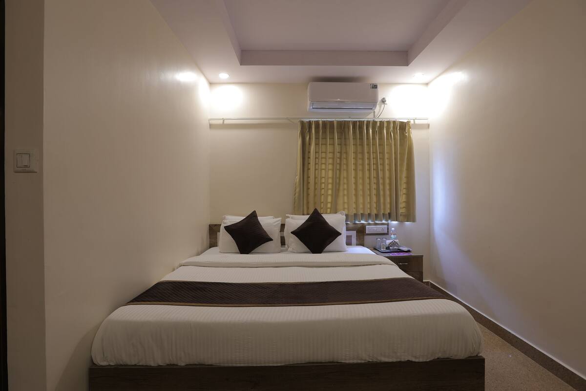 Une chambre d’hôtel bien aménagée, avec un grand lit, une table de chevet, un appareil de climatisation et une fenêtre avec des rideaux.