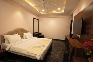 Een moderne hotelkamer met een groot bed, een houten dressoir, een flatscreen televisie en een plafondventilator.