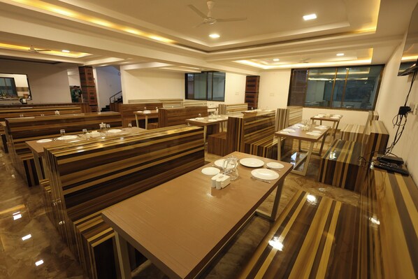 Un comedor moderno con mesas y bancos de madera y vidrio, y una cocina al fondo.