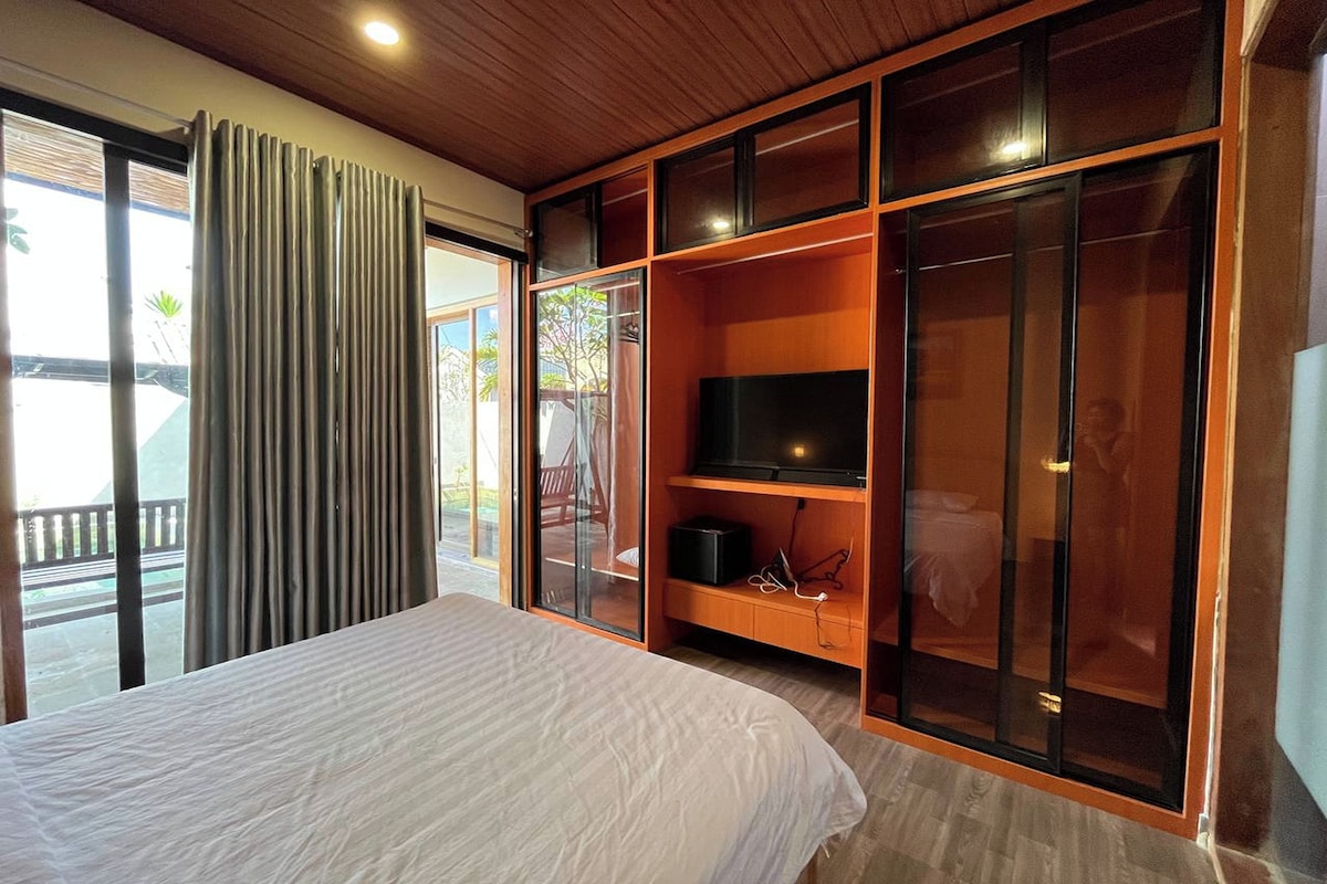 A bedroom with a bed, a TV, and a sliding glass door leading to a balcony.