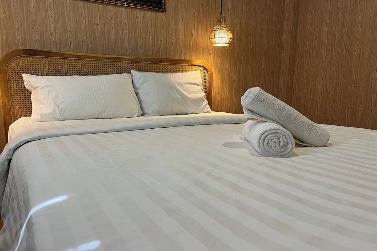 A neatly made bed with white linens and pillows, a rolled towel on the bed, and a hanging light fixture above.