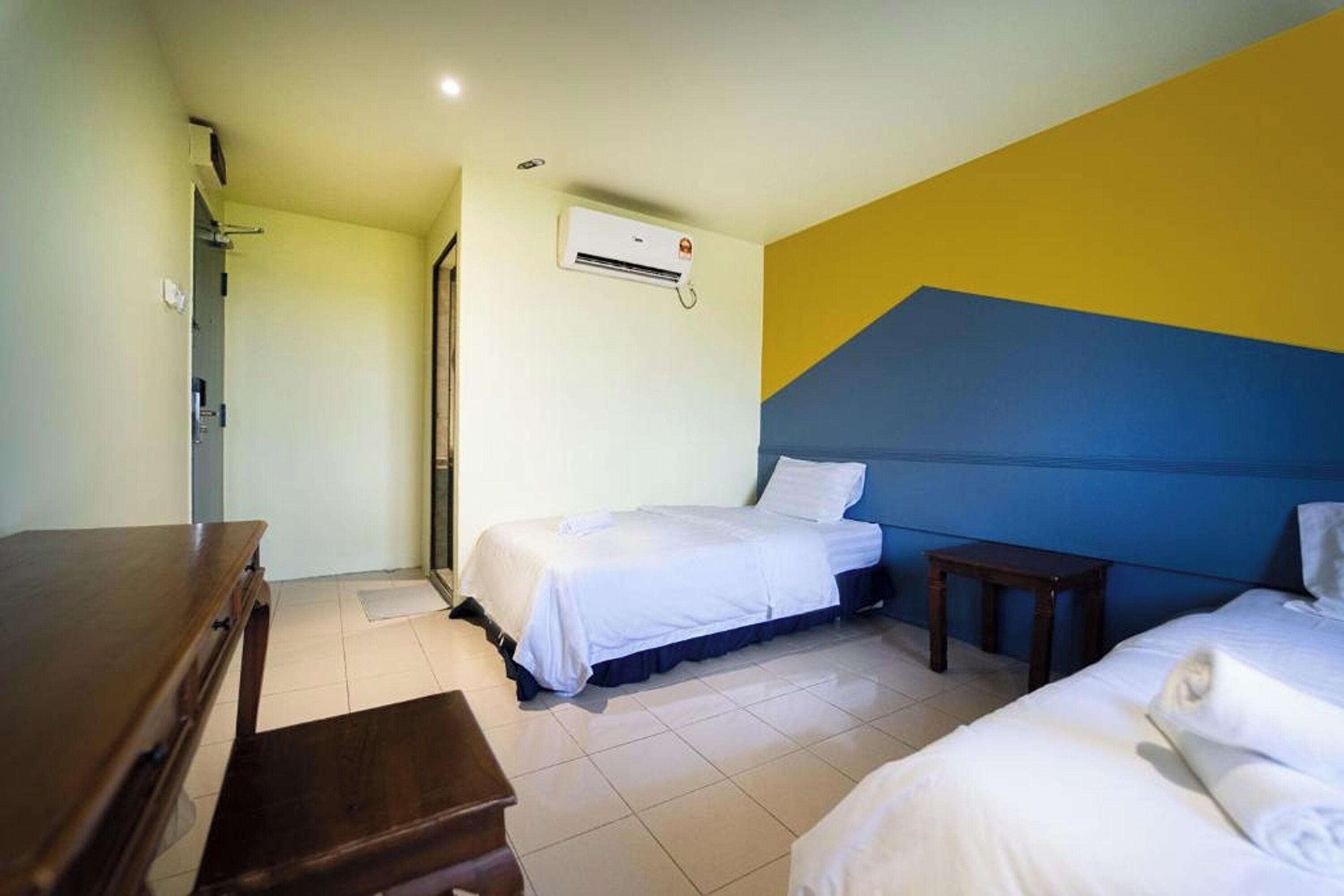 A hotel room with two beds, a wooden dresser, and an air conditioning unit on the wall.