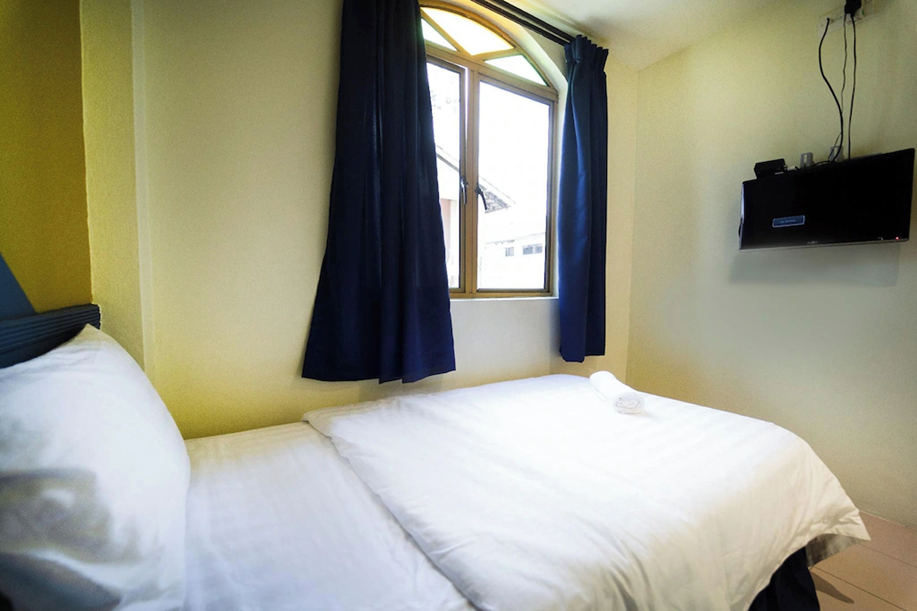 A hotel room with a bed, a window with curtains, and a mounted television.