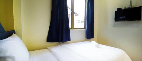 Una habitación de hotel con cama, ventana con cortinas y televisor montado.