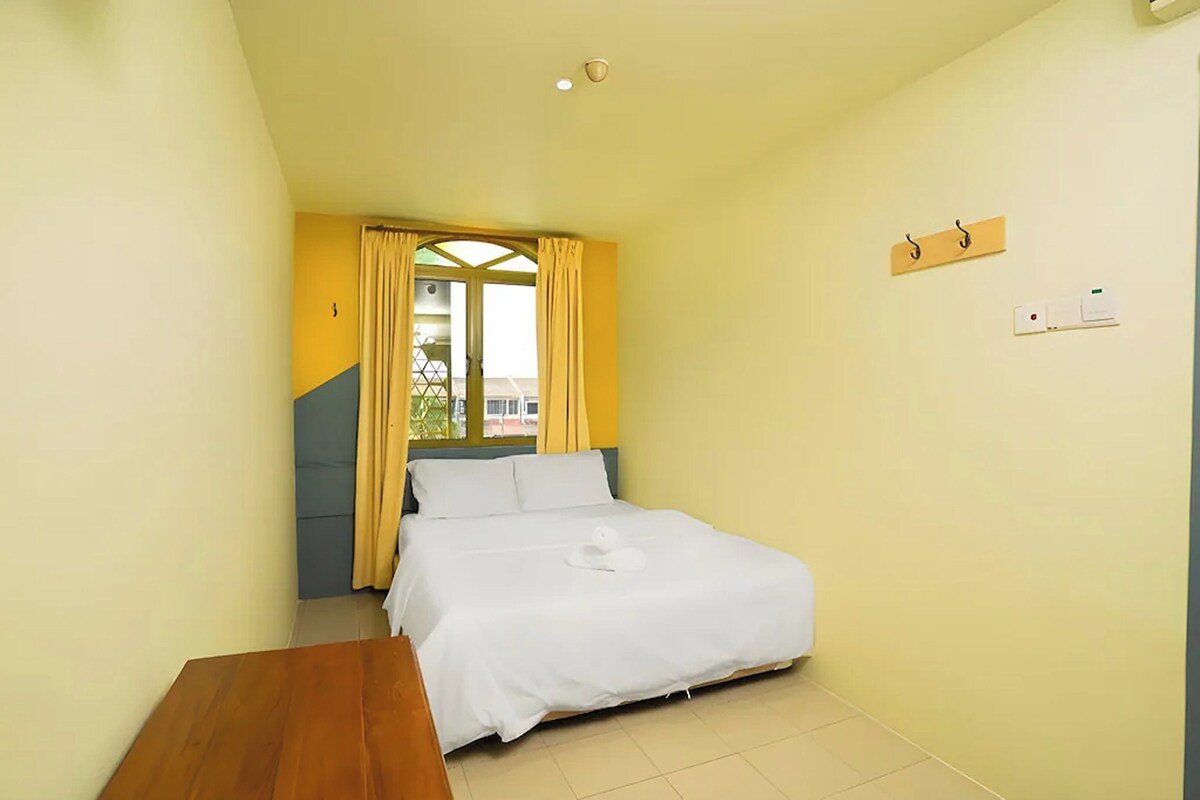 A bedroom with a bed, a wooden table, a window with curtains, and a wall-mounted light fixture.