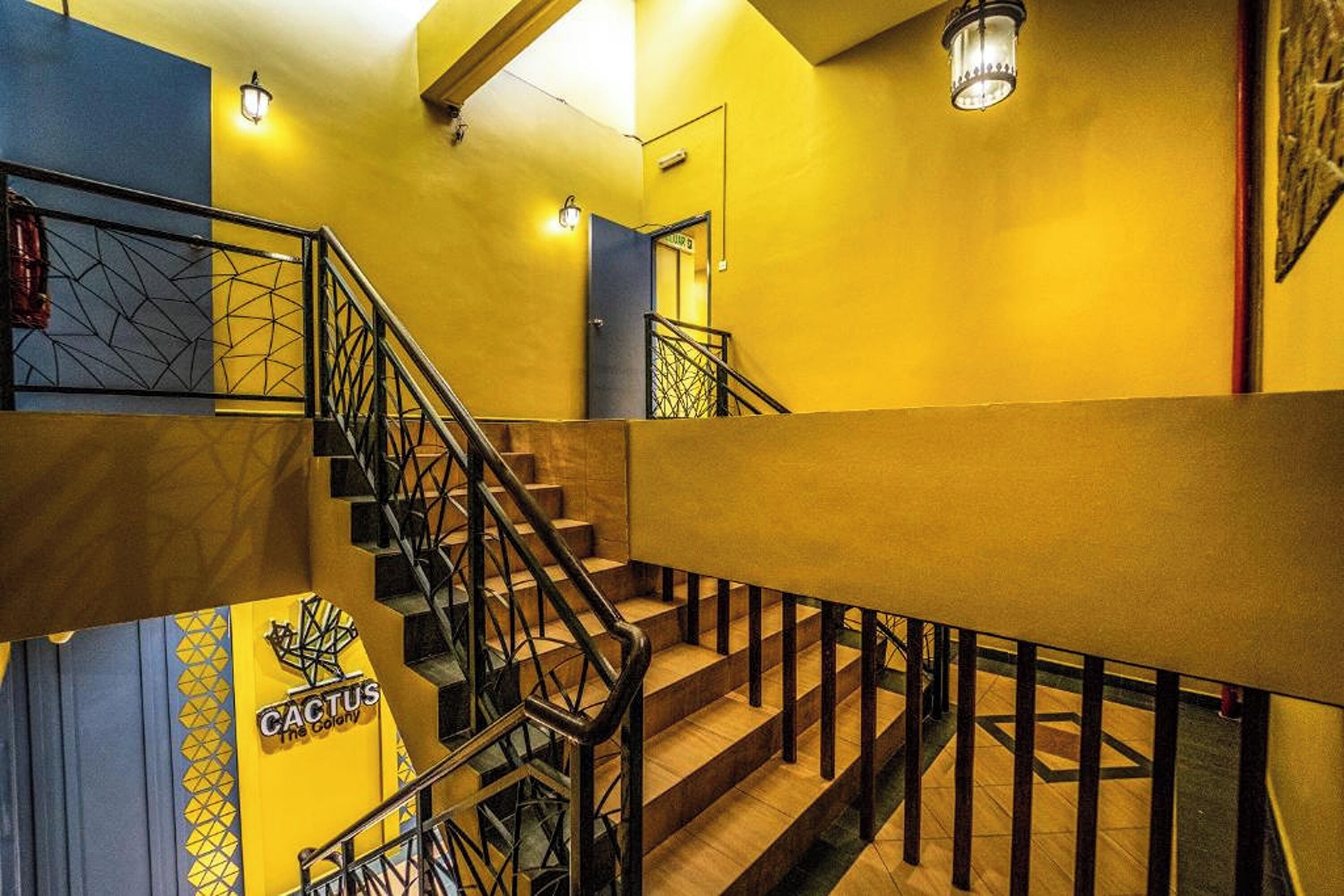 A staircase with a geometric railing design, a yellow wall, and a sign reading "Cactus The Colony".
