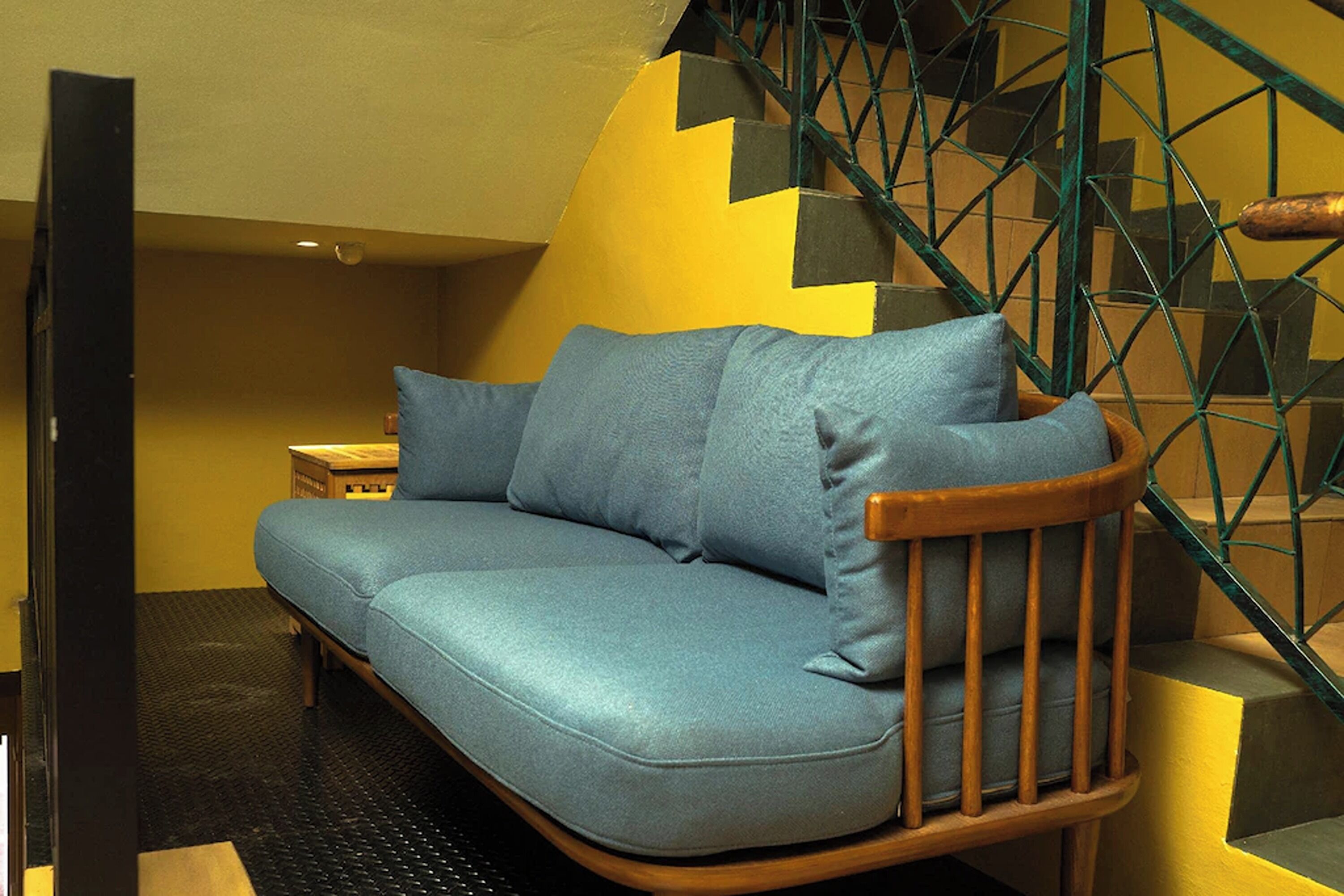 A blue sofa in a room with a staircase and a wooden floor.