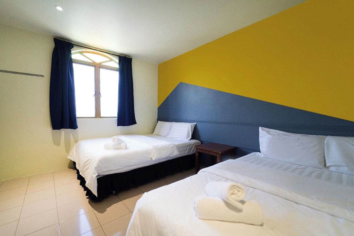 A hotel room with two beds, a window with curtains, and a yellow accent wall.