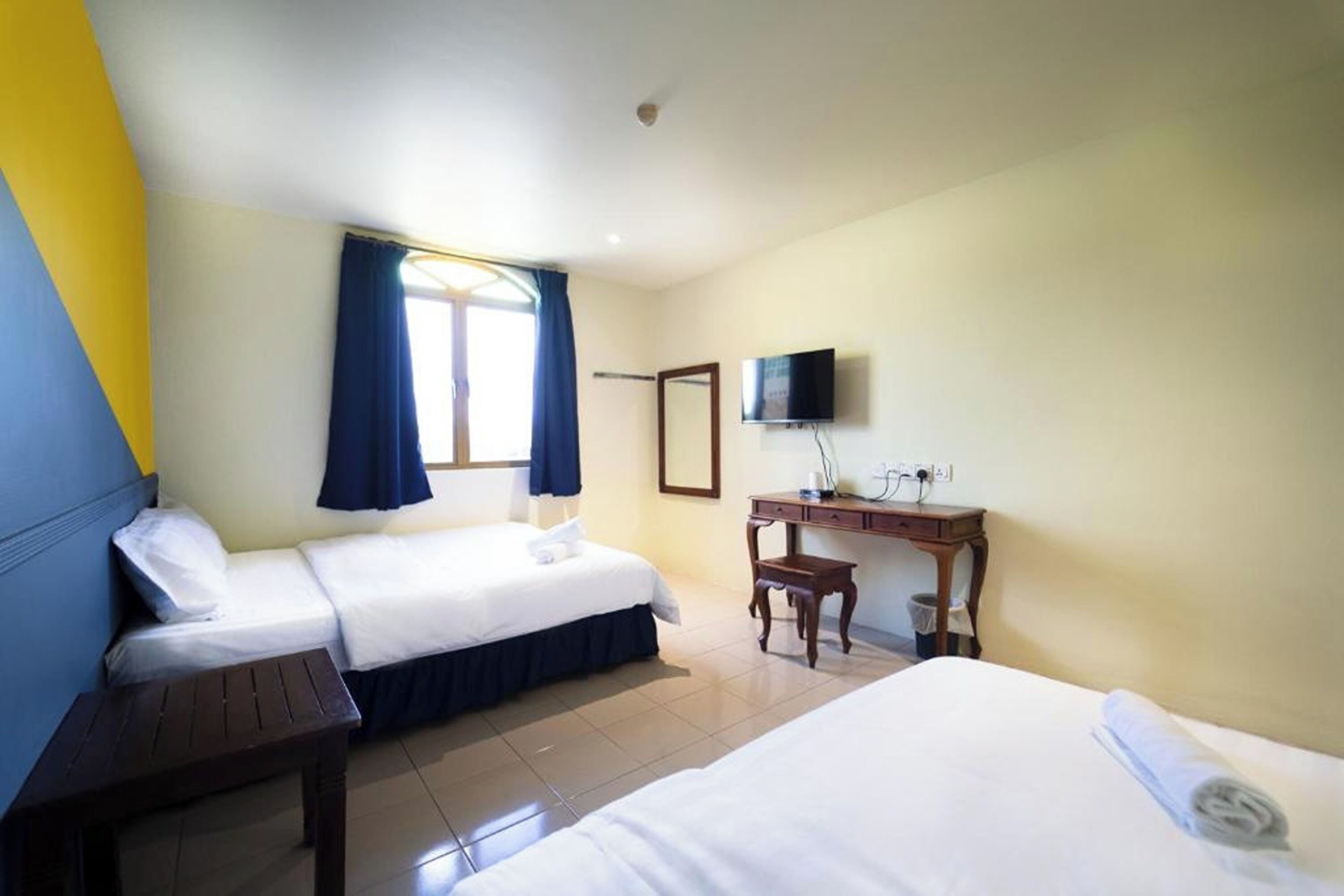Habitación de hotel con dos camas, un escritorio, televisión y ventana con cortinas.