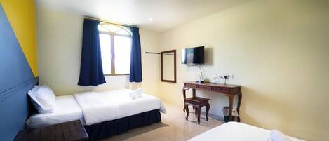 Habitación de hotel con dos camas, un escritorio, televisión y ventana con cortinas.