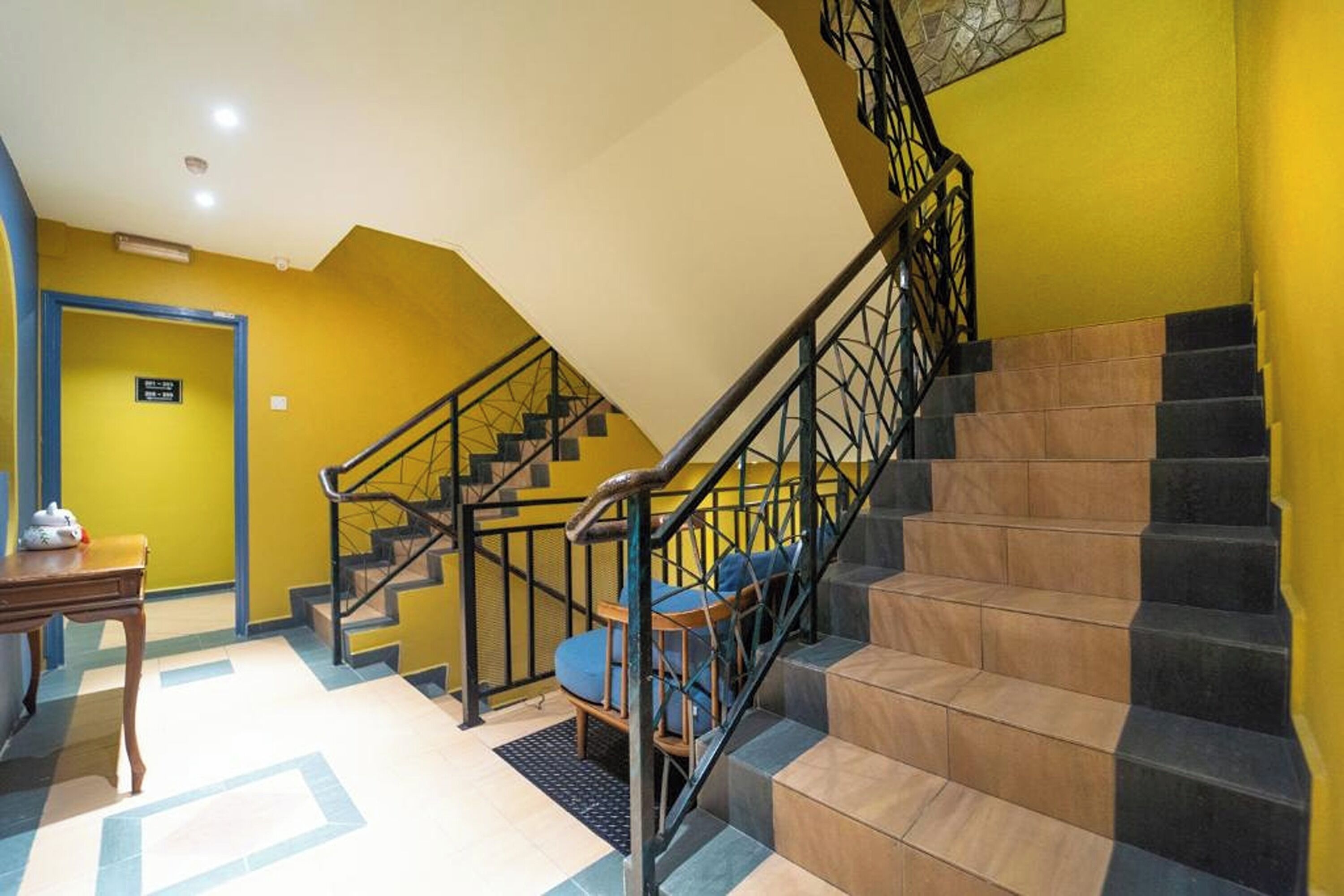A staircase with black railings and blue cushioned steps, leading to a room with yellow walls and a wooden table.
