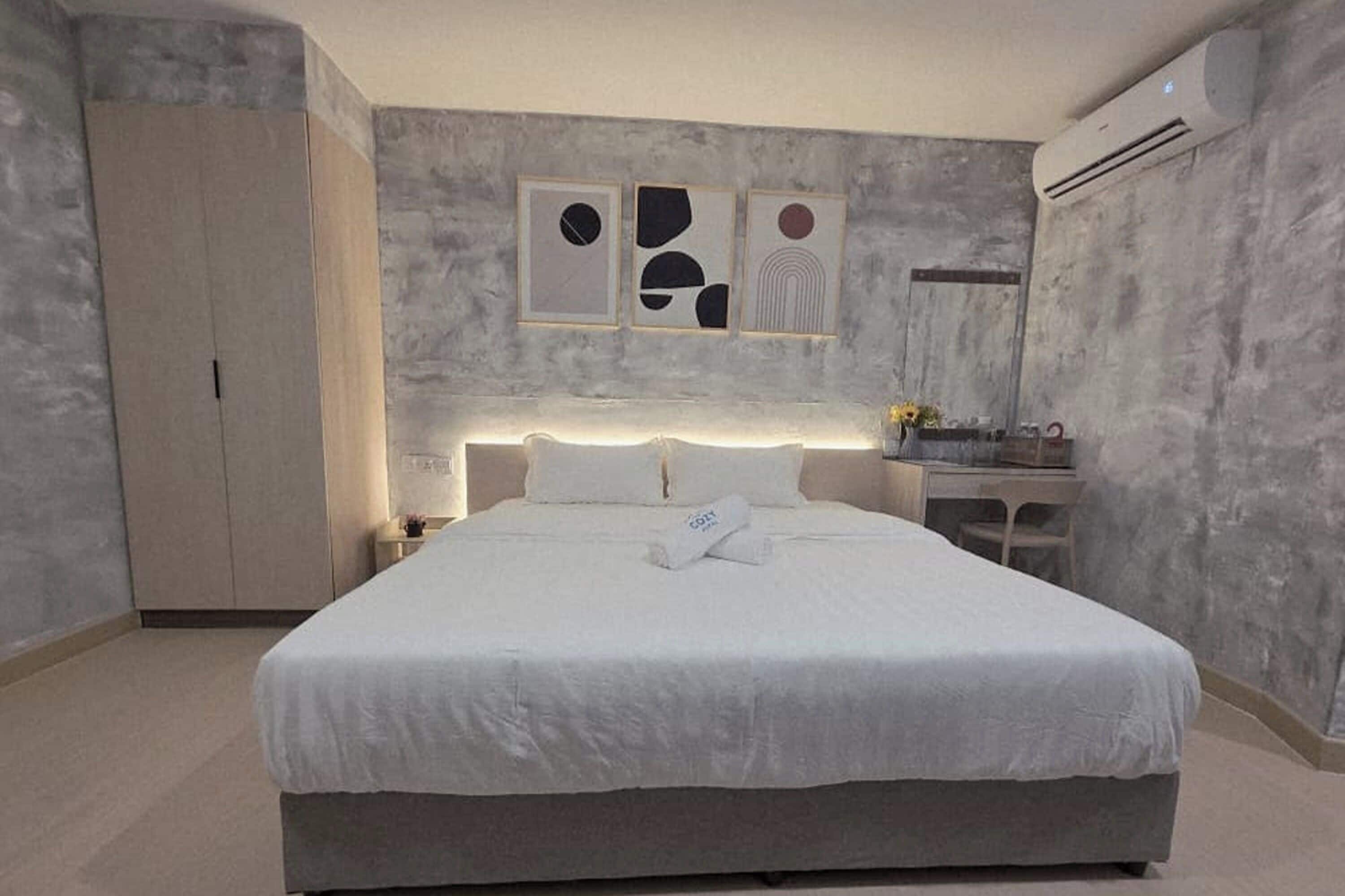 Una habitación de hotel moderna con una cama grande, un armario, un escritorio con silla y cuadros en la pared.