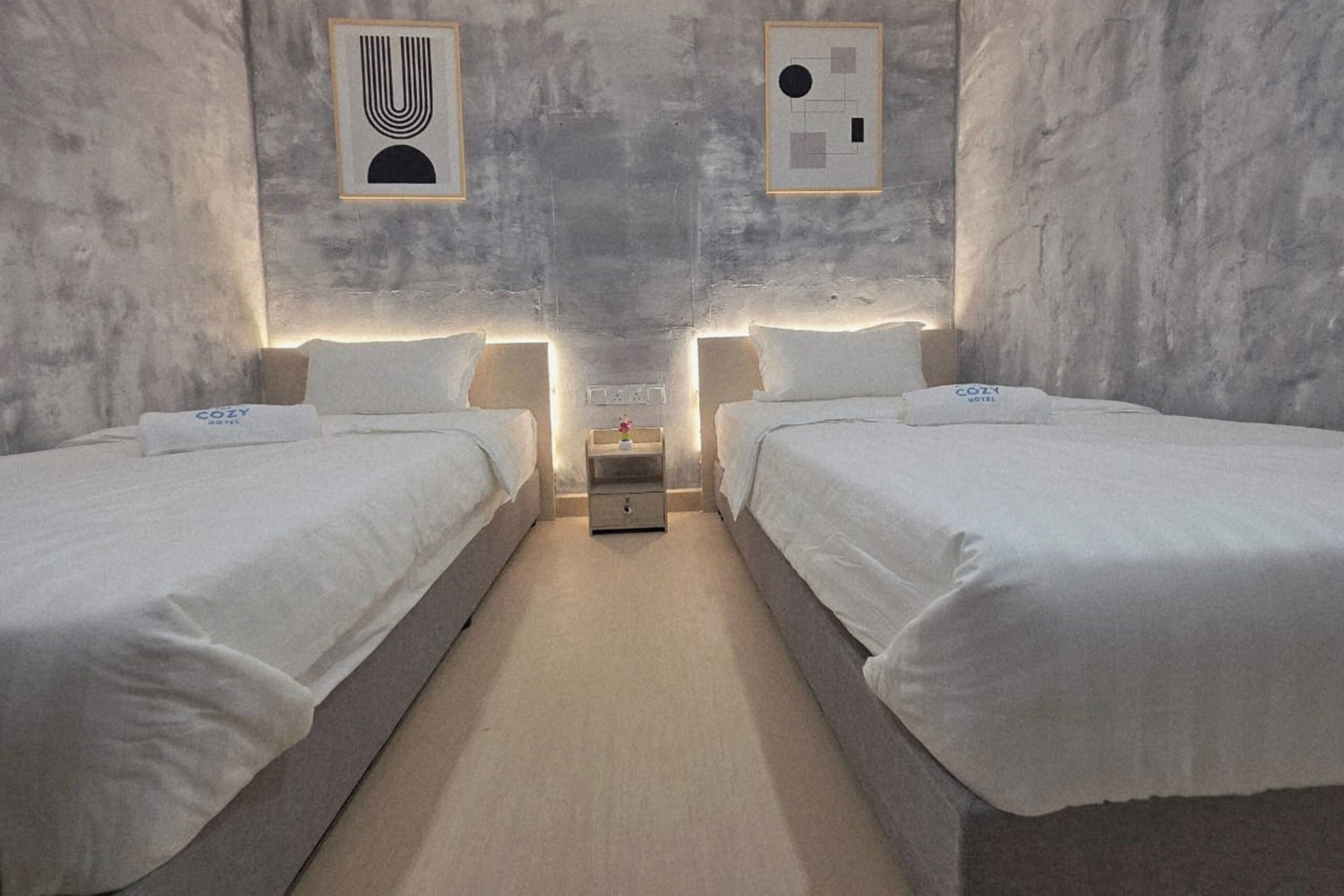 A hotel room with two beds, a nightstand, and a wall-mounted light fixture.