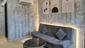 Un salon moderne avec un canapé gris, une table ronde et des œuvres d’art abstraites accrochées au mur.