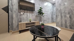 Un salon moderne avec un téléviseur à écran plat fixé au mur, une table ronde noire et deux plantes en pot.