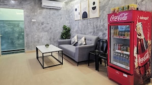 Un hall d’entrée moderne avec un canapé gris, une petite table, un réfrigérateur rouge de la marque Coca-Cola et un panneau indiquant « SORTIE ».