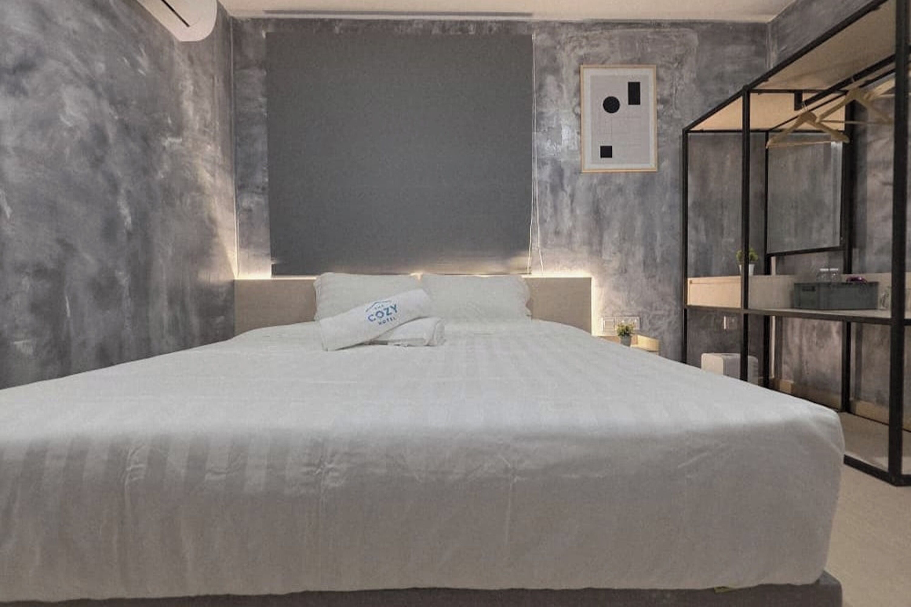 A modern bedroom with a large bed, a bedside table, a wall-mounted light, and a built-in shelving unit.