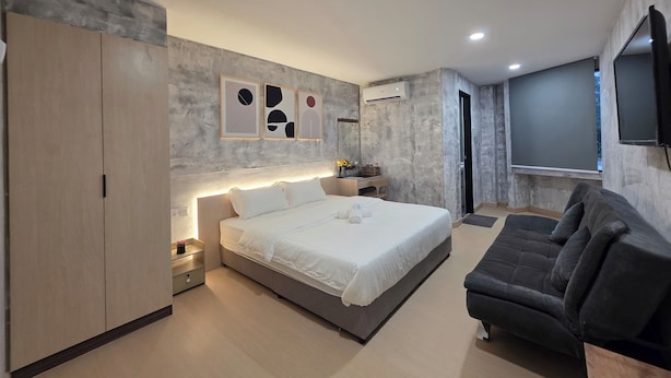 Une chambre à coucher moderne avec un lit, un canapé foncé, une armoire, une table de chevet et un téléviseur fixé au mur.
