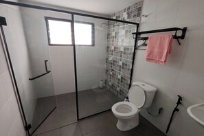 A bathroom with a glass-enclosed shower, a toilet, a sink, and a towel rack with a pink towel. - Drh Villa (Ipoh)