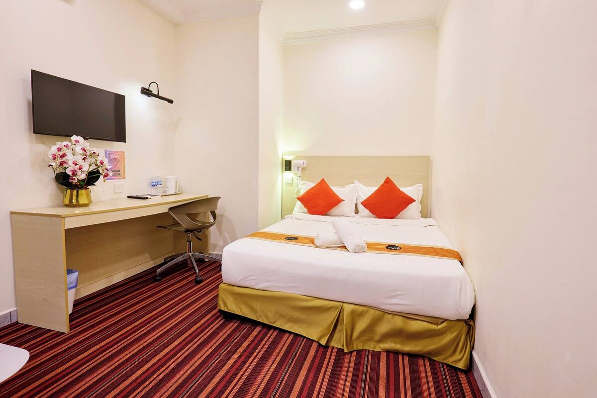 Ein Hotelzimmer mit Bett, Schreibtisch, Stuhl und einem an der Wand befestigten Flachbildfernseher.