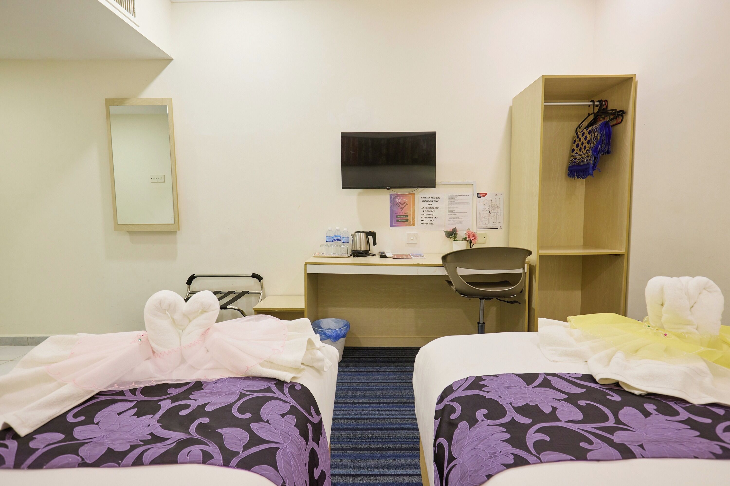 Une chambre d’hôtel avec deux lits, un bureau, une chaise, une télévision, une armoire et une poubelle.
